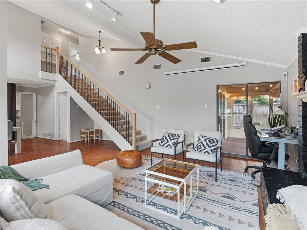 2812 Prescott Drive, Carrollton, TX 75006 Spacious living area featuring vaulted ceilings, wood-finish flooring, and a multi-level staircase with carpeted treads and metal balusters