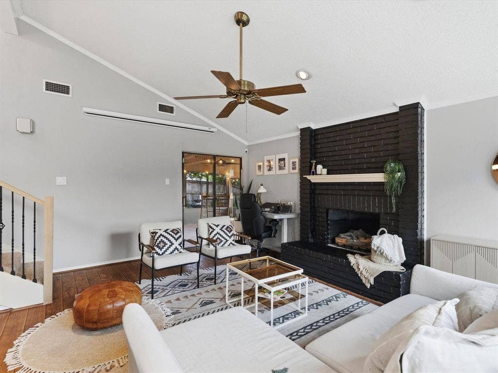2812 Prescott Drive, Carrollton, TX 75006 Vaulted ceiling living space featuring a dark brick fireplace with a mantle, wood-finish flooring, a ceiling fan, and black-framed glass patio doors