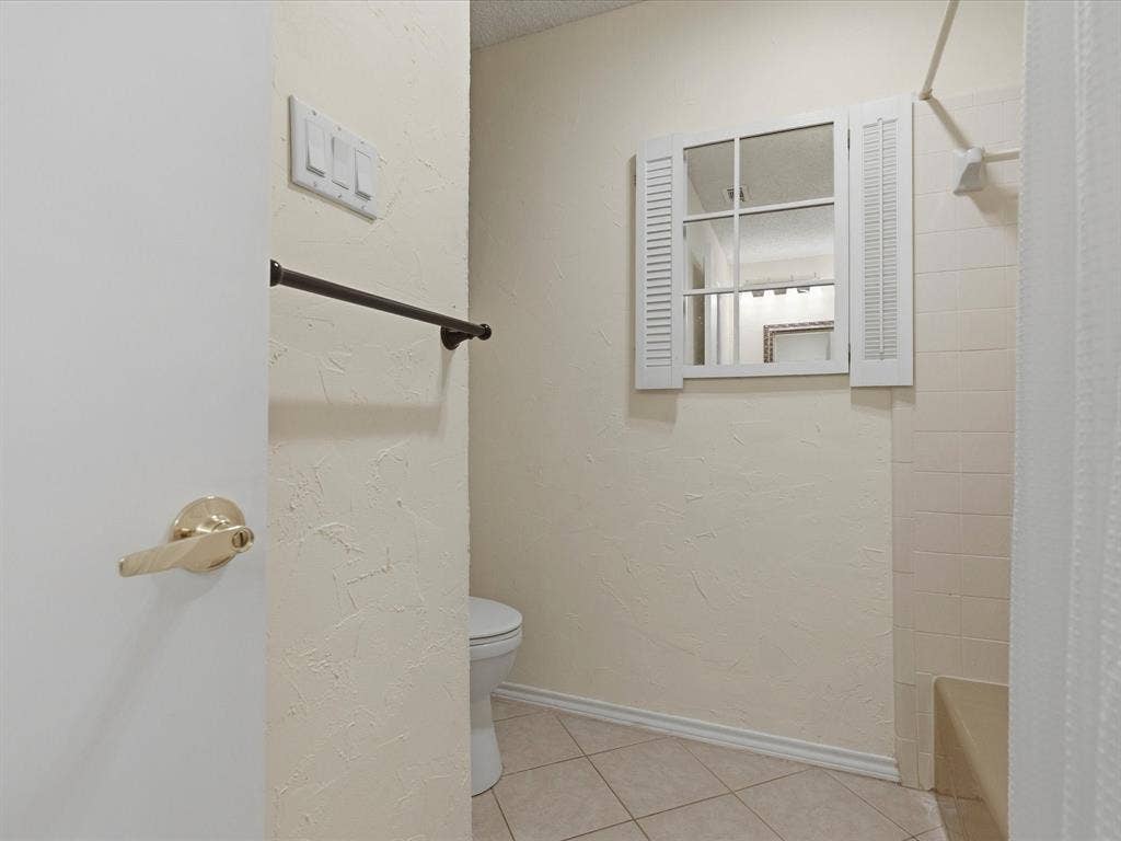 2812 Prescott Drive, Carrollton, TX 75006 Bathroom featuring a window-style mirror with decorative shutters, tiled flooring, textured walls, a shower with tiled surround, and a built-in shower bench