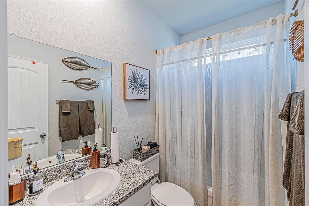 Bathroom featuring a vanity with a granite-style countertop, an undermount sink with a chrome faucet, a large wall-mounted mirror, and a shower with a white curtain