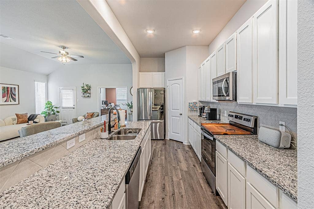 Kitchen featuring granite countertops, wood-finish flooring, stainless steel appliances, white cabinetry, and a tile backsplash