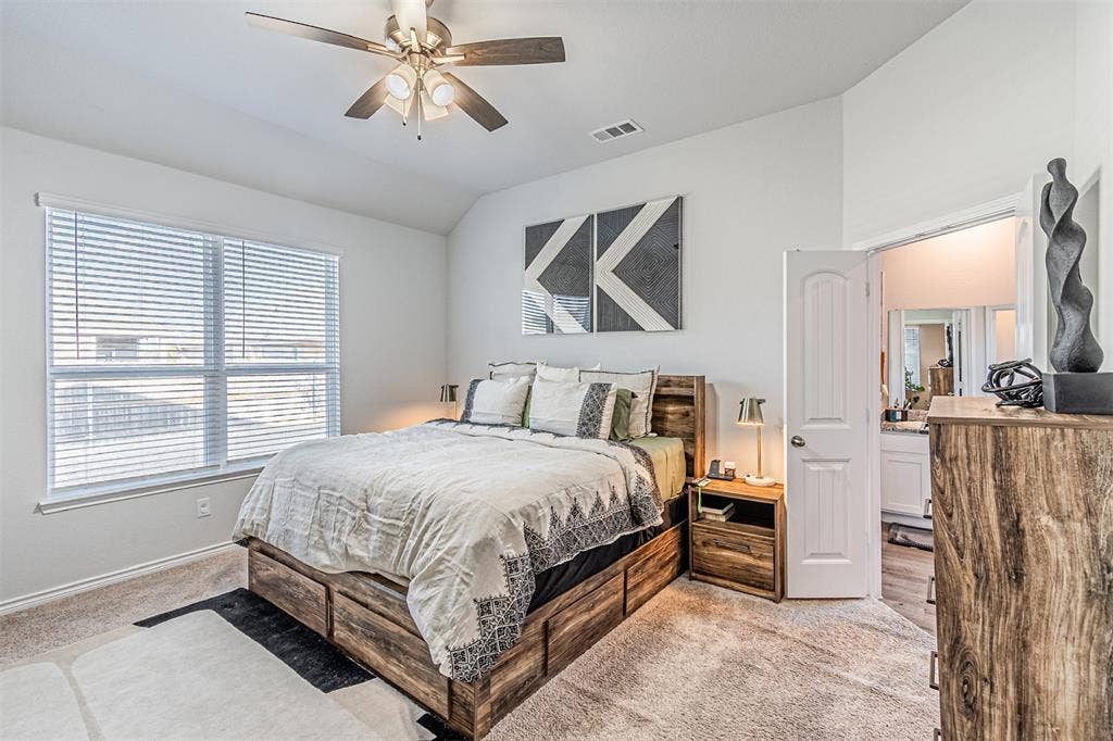 Carpeted bedroom featuring vaulted ceilings, a ceiling fan with light kit, and a window with blinds