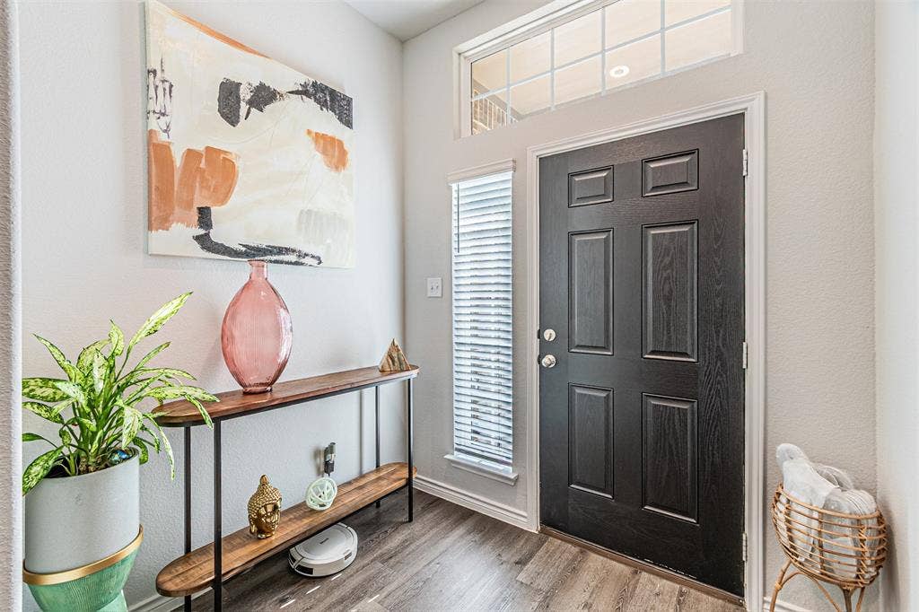 Entryway featuring a dark paneled door with brushed nickel hardware, wood-finish flooring, a sidelight window with blinds, and a transom window