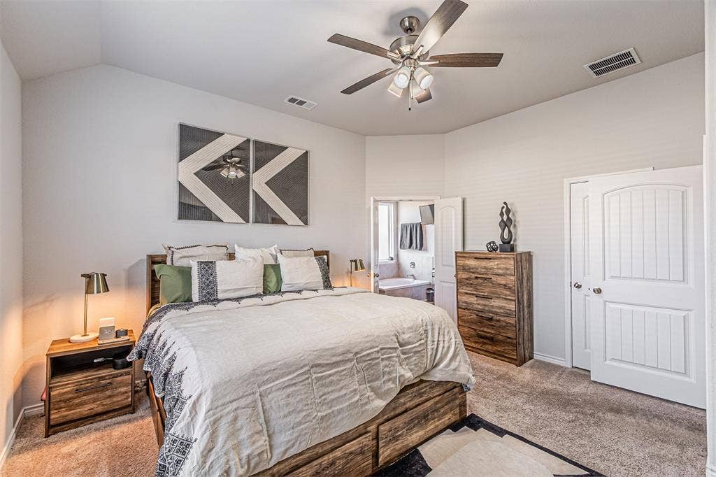 Carpeted bedroom featuring vaulted ceilings, a ceiling fan with integrated lighting, and a paneled interior door
