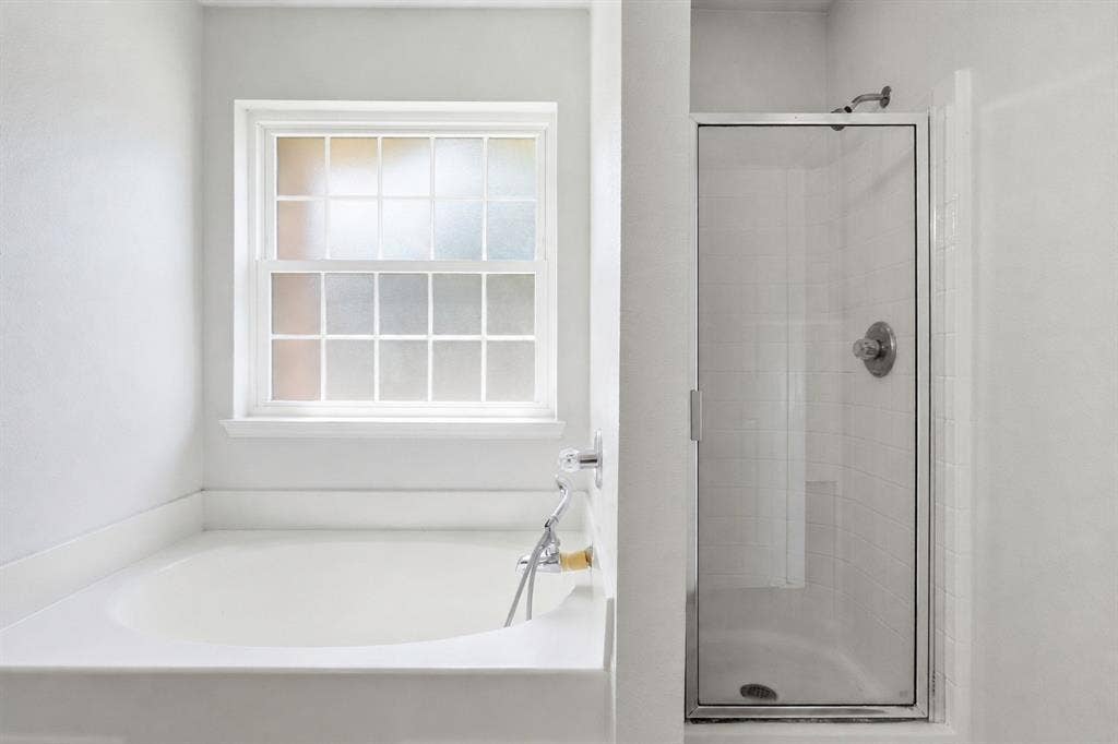 Bathroom featuring a built-in soaking tub with chrome fixtures, a frosted glass window, and a glass-enclosed shower with a chrome showerhead