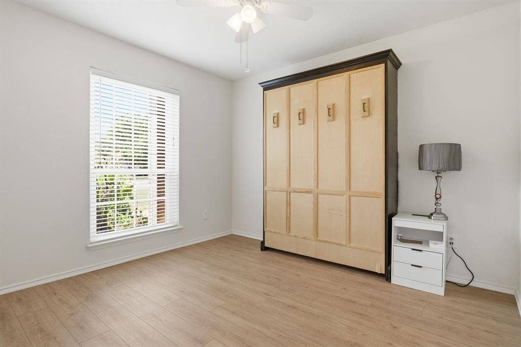 Bright room featuring a built in murphy bed,  large window with horizontal blinds, wood-finish flooring, and a ceiling fan