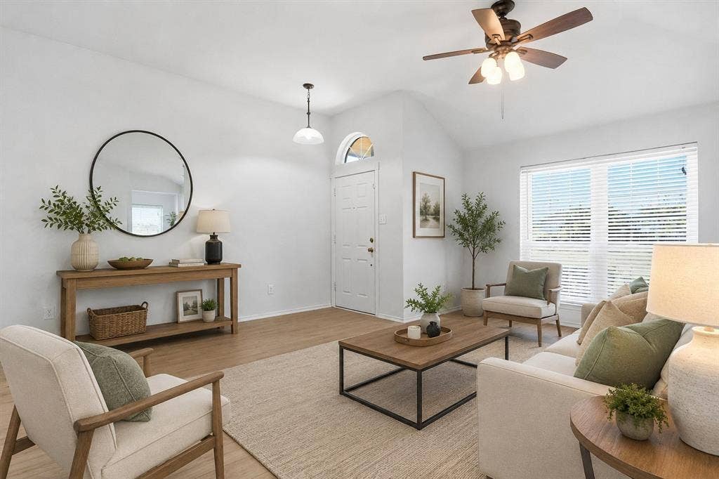 Vaulted ceiling living/entry space featuring wood-finish flooring, a contemporary ceiling fan, and a large window with horizontal blinds. *Picture is virtually staged using AI
