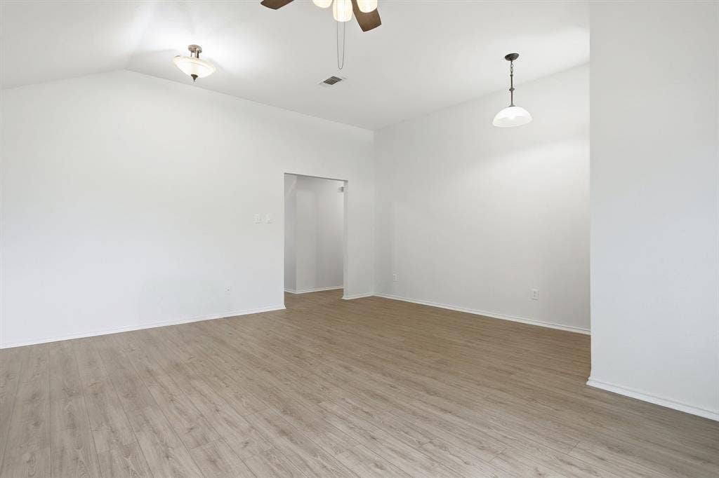 Spacious room featuring wood-finish flooring, vaulted ceiling, and white wall finishes
