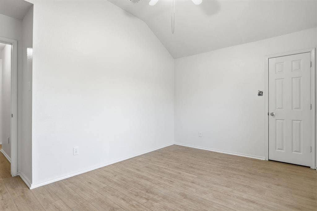 Vaulted ceiling room featuring wood-finish flooring, white baseboards, and a ceiling fan