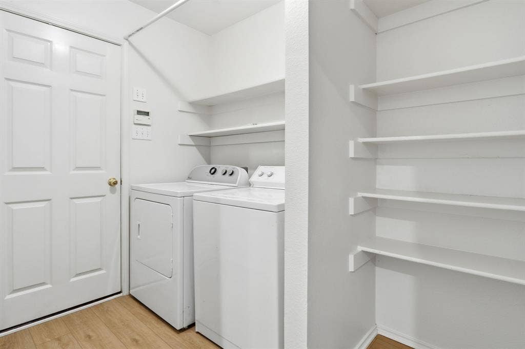 Dedicated laundry area featuring a washer and dryer, wood-finish flooring, built-in shelving, and white paneled door