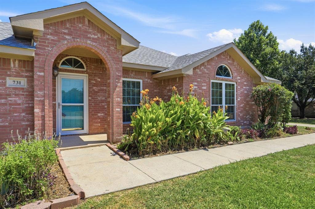 Brick facade residence featuring an arched entryway, gabled roofline, and mature landscaping