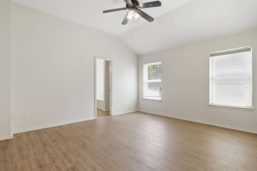Spacious room featuring vaulted ceilings, wood-finish flooring, and a ceiling fan