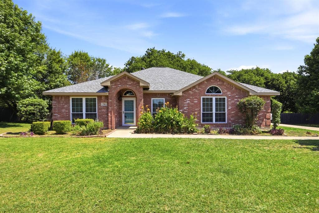 Brick facade residence featuring an arched entryway, gabled roofline, and mature landscaping
