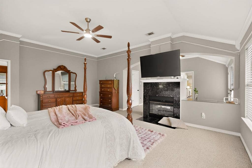 712 Water Oak Drive, Plano, TX 75025 Carpeted bedroom featuring a black stone fireplace surround, high vaulted ceilings, crown molding, and a ceiling fan with integrated lighting