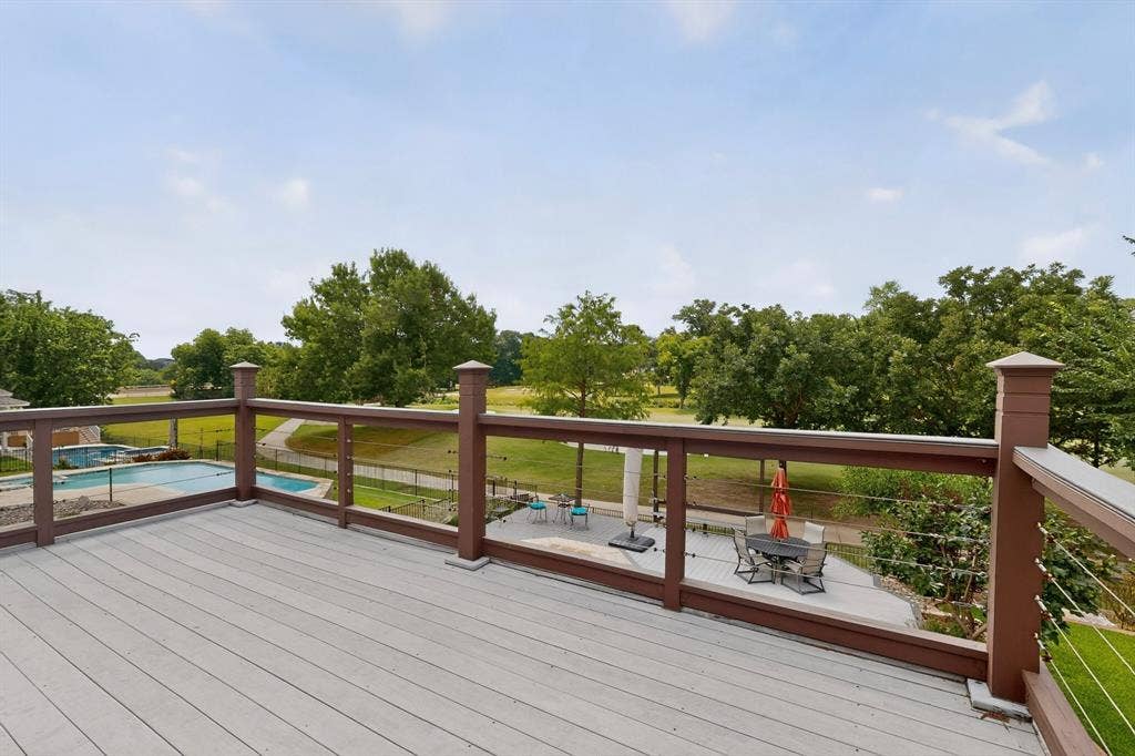 712 Water Oak Drive, Plano, TX 75025 Elevated wood-finish deck with cable railing overlooking a landscaped backyard featuring a swimming pool, concrete patio, and mature trees