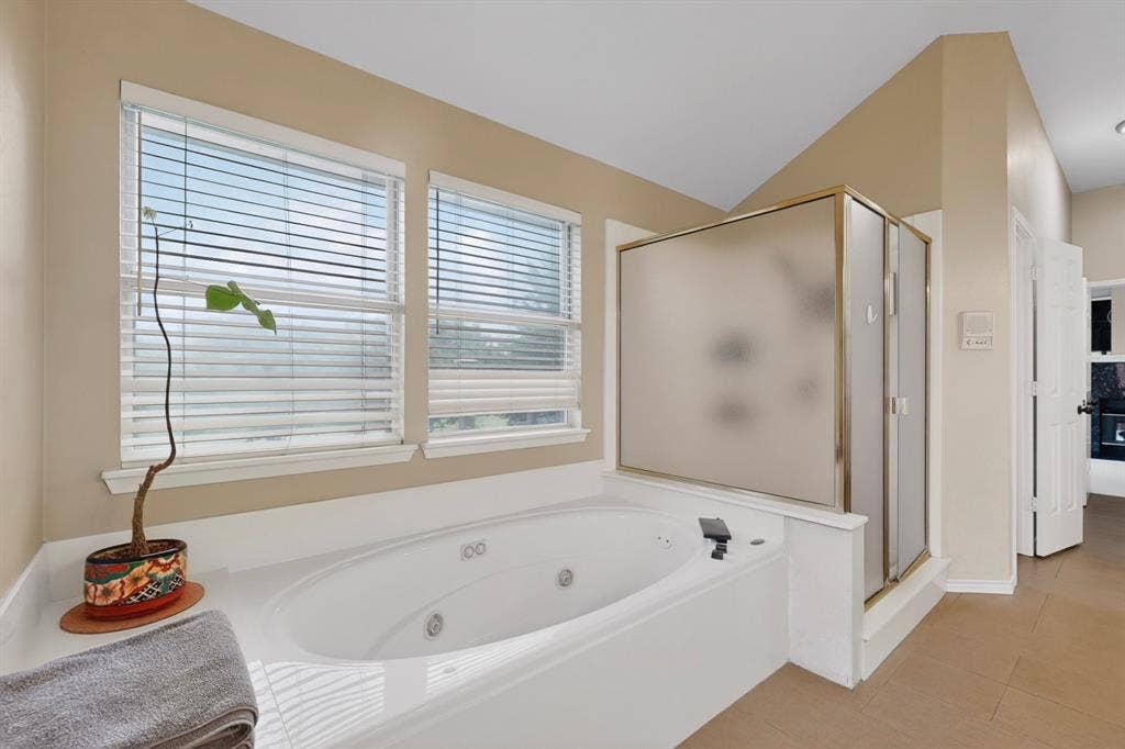 712 Water Oak Drive, Plano, TX 75025 Built-in soaking tub with white surround, two horizontal windows, and a glass-enclosed shower with a gold-tone frame