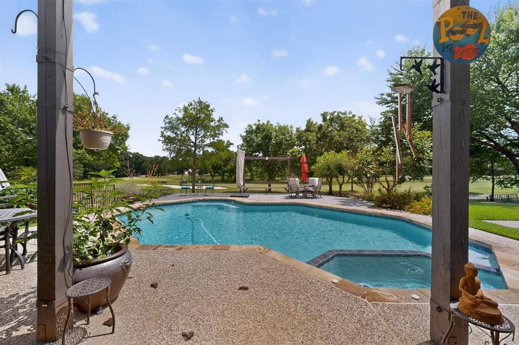 712 Water Oak Drive, Plano, TX 75025 Outdoor living area featuring an in-ground swimming pool with an integrated spa, expansive exposed aggregate patio, and mature trees