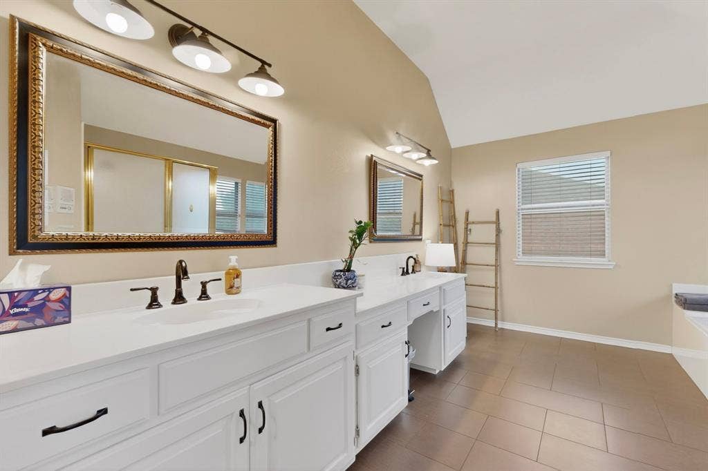 712 Water Oak Drive, Plano, TX 75025 Double vanity with white cabinetry, matte black hardware, and an ornate framed mirror