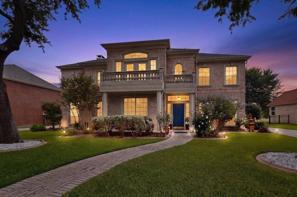 712 Water Oak Drive, Plano, TX 75025 Brick facade residence featuring a second-story balcony with balustrade, arched window accents, and a contrasting blue front door
