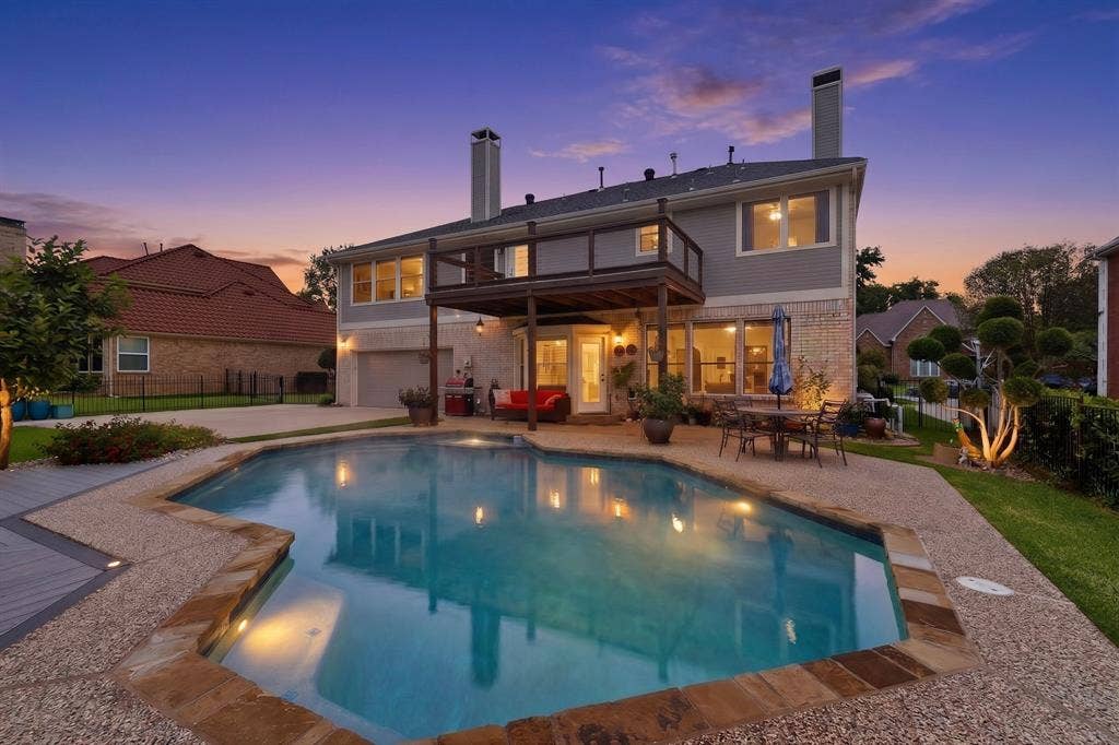 712 Water Oak Drive, Plano, TX 75025 Rear exterior featuring a freeform swimming pool with stone coping, an upper-level deck, a lower-level patio, and a two-story residence with brick and siding finishes
