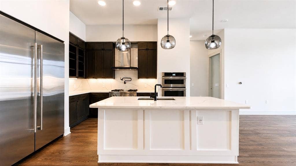 3330 Oak Grove Avenue, #1307, Dallas, TX 75204 Modern kitchen featuring a large white island with a matte black faucet, dark wood cabinetry, stainless steel appliances, and wood-finish flooring