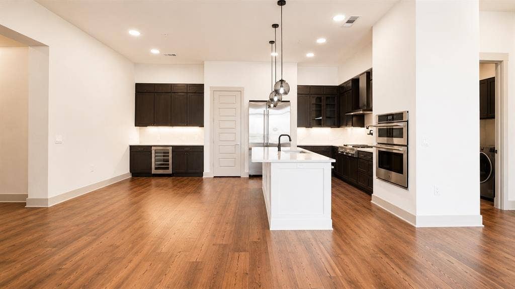 3330 Oak Grove Avenue, #1307, Dallas, TX 75204 Open-concept kitchen featuring wood-finish flooring, a central island with a white countertop, dark cabinetry, and stainless steel appliances, including double wall ovens