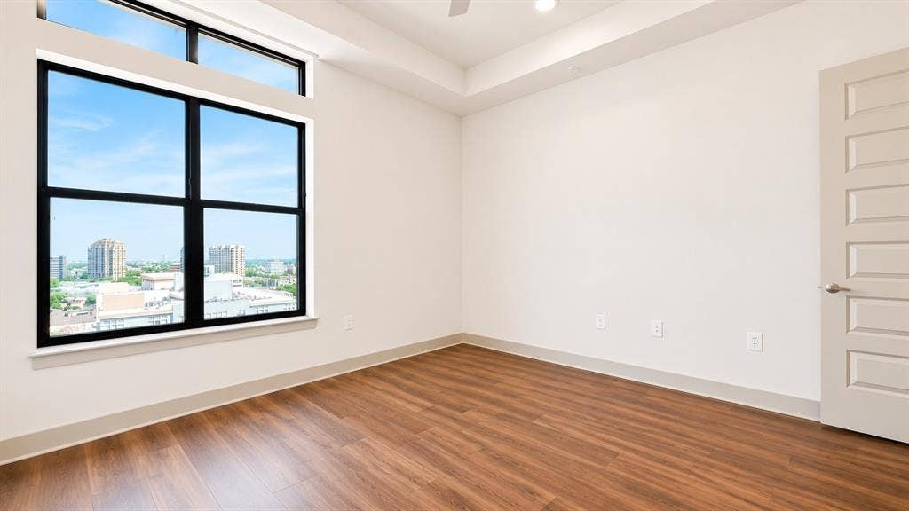 3330 Oak Grove Avenue, #1307, Dallas, TX 75204 Expansive window with black framing and transom window, wood-finish flooring, white walls, tray ceiling, and a five-panel interior door