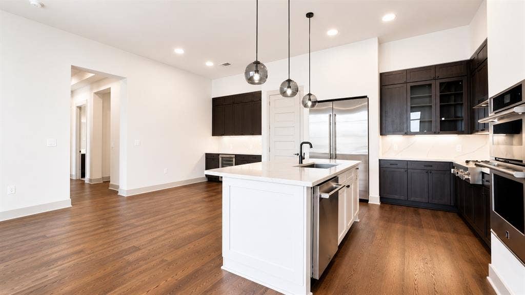 3330 Oak Grove Avenue, #1307, Dallas, TX 75204 Gourmet kitchen featuring a central island with a white countertop and seating, dark wood-finish cabinetry, stainless steel appliances, and wood-finish flooring