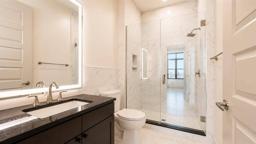 3330 Oak Grove Avenue, #1307, Dallas, TX 75204 Contemporary bathroom featuring a dark wood vanity with a black countertop and an integrated sink, illuminated by a backlit mirror