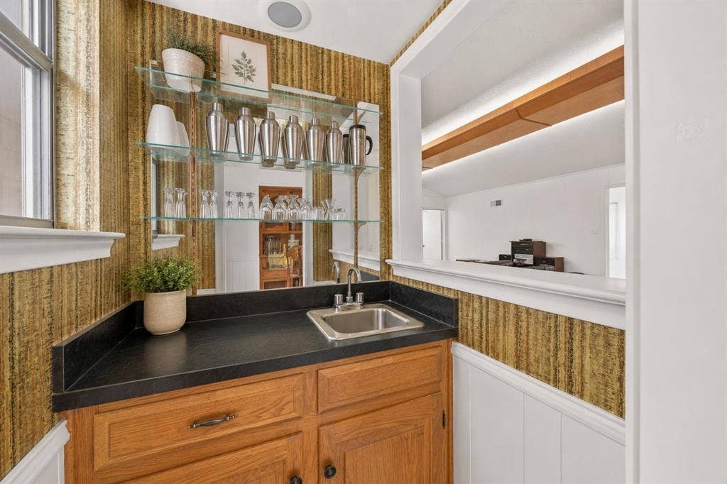 2125 Woodbrook Street, Denton, TX 76205 Wet bar featuring a stainless steel sink, dark countertop, and wood cabinetry