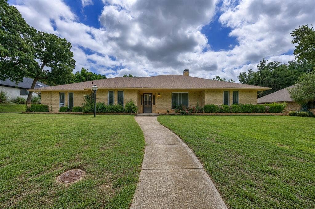 2125 Woodbrook Street, Denton, TX 76205 Ranch-style residence featuring a light brick exterior, a tan shingle roof, and a prominent front walkway