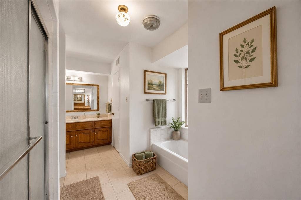 2125 Woodbrook Street, Denton, TX 76205 Bathroom featuring a built-in shower with frosted glass doors, a vanity with wood-finish cabinetry and a stone-finish countertop, a large framed mirror, a built-in bathtub with white tile surround, and neutral tile flooring