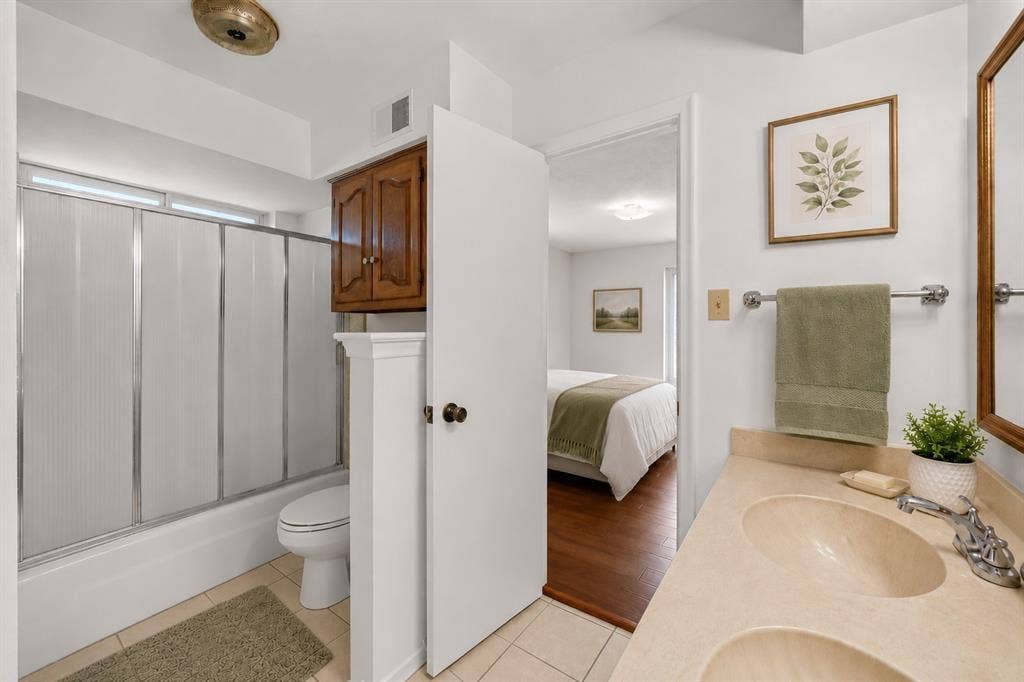 2125 Woodbrook Street, Denton, TX 76205 Bathroom featuring a double vanity with built-in sinks, a wall-mounted mirror, and a combination shower/tub with sliding glass panels