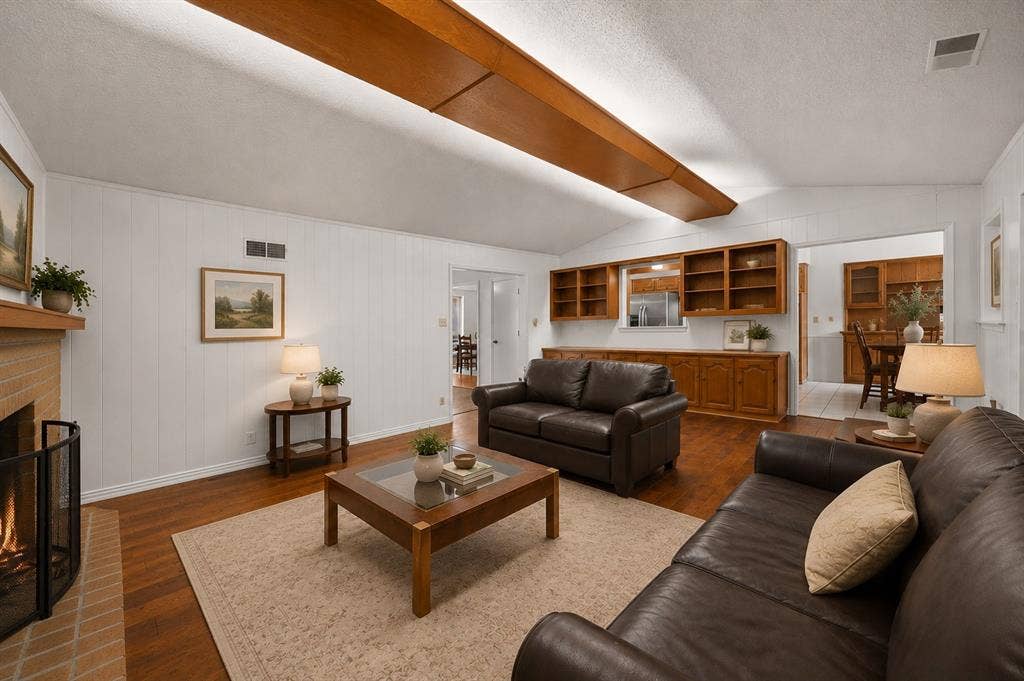 2125 Woodbrook Street, Denton, TX 76205 Vaulted ceiling with wood-finish beam accents, brick fireplace with a hearth, wood-finish flooring, built-in shelving and cabinetry, and white vertical paneling