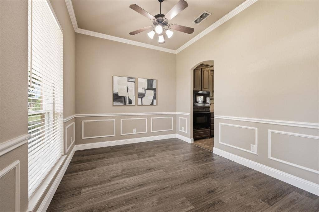Spacious interior room featuring wood-finish flooring, wainscoting, crown molding, and a ceiling fan with integrated lighting