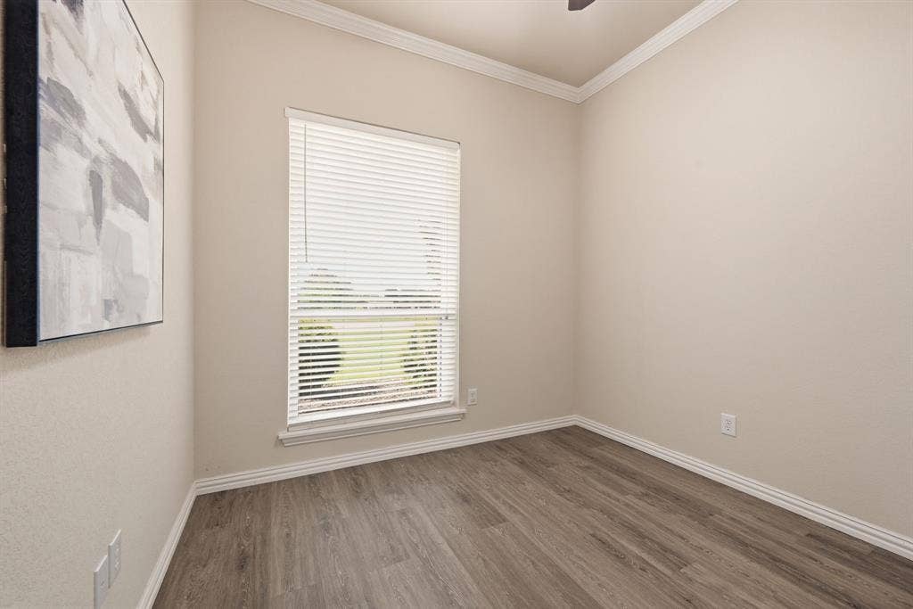 Bedroom featuring neutral-toned walls, wood-finish flooring, white baseboards, and white crown molding