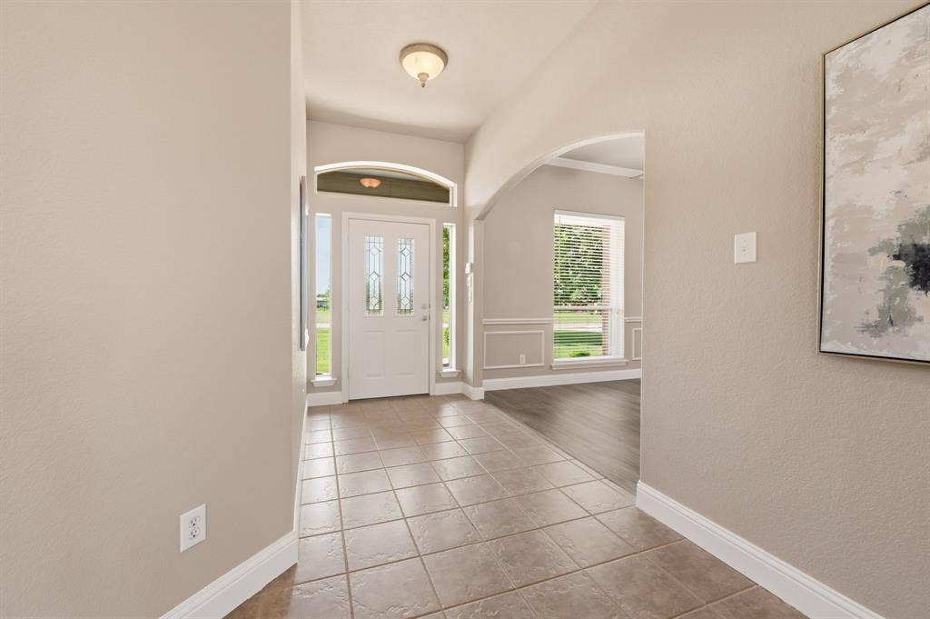 Entryway featuring tile flooring, a decorative glass front door with sidelights and transom, an arched doorway, and light wall tones