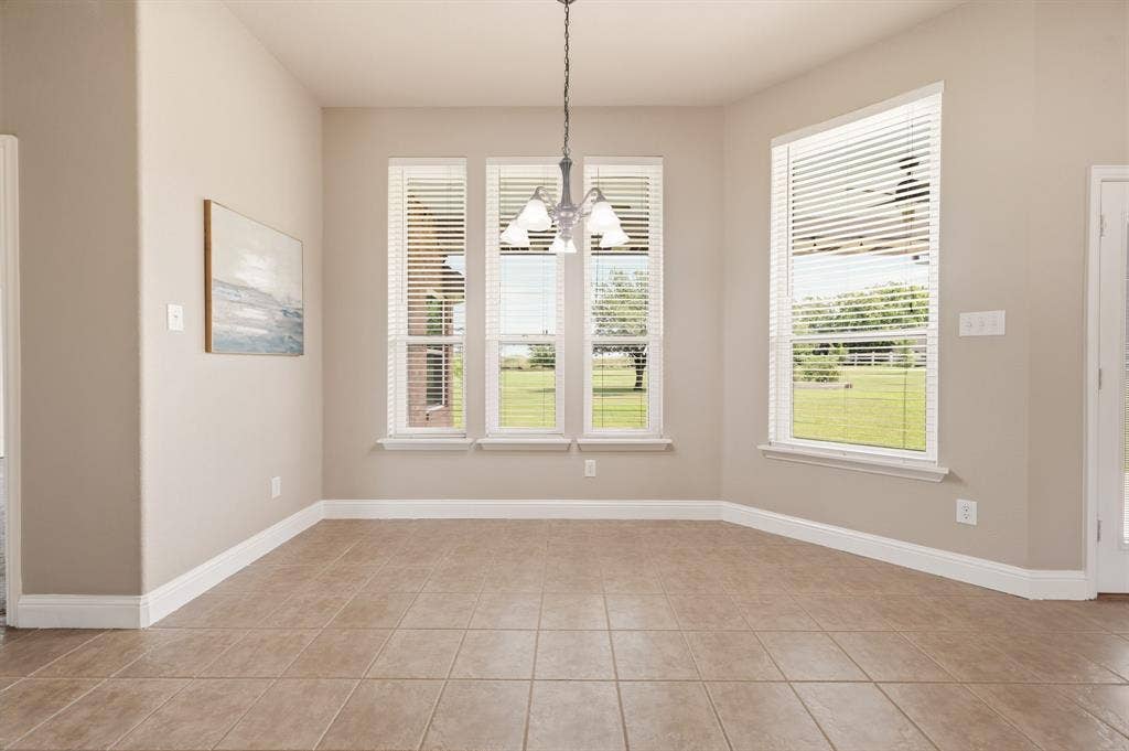Room featuring large-format tile flooring, multiple windows with blinds, a ceiling-mounted light fixture, and neutral-toned walls with white trim