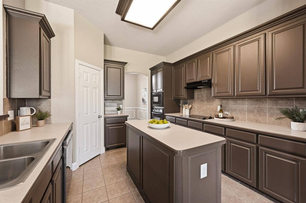 Kitchen featuring dark wood cabinetry, light countertops, a central island, stainless steel double basin sink, and integrated wall oven
