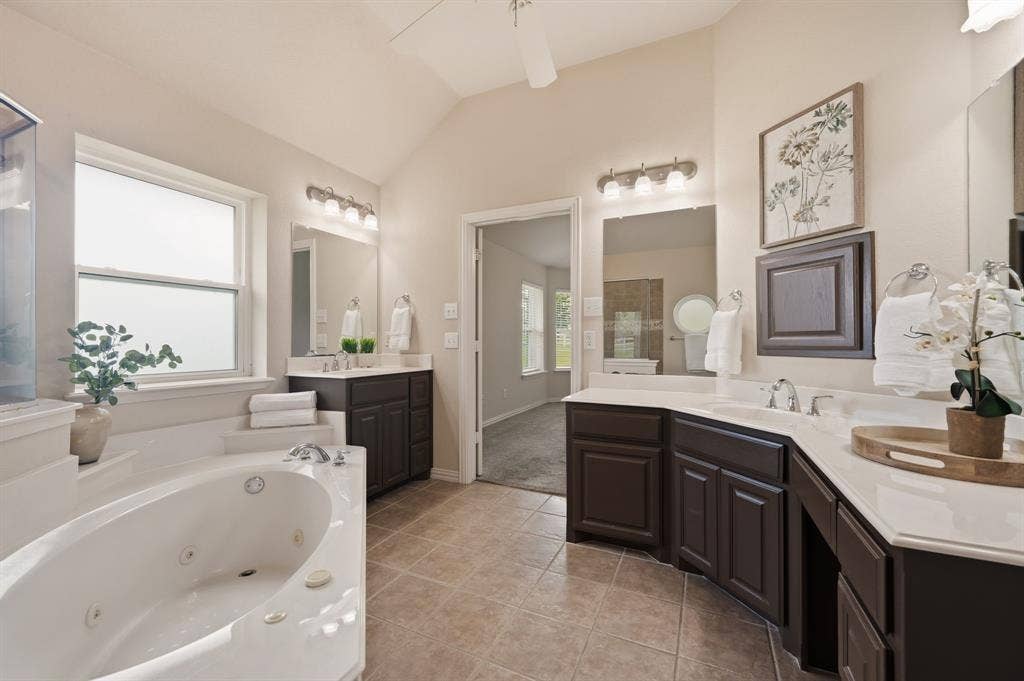 Spacious bathroom featuring a large jetted tub, dual window, dual vanities with integrated sinks, dark wood-finish cabinetry, and tiled flooring