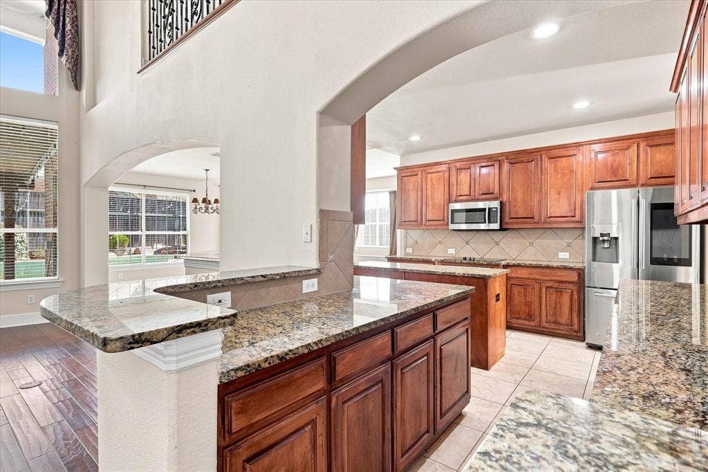 509 Wentworth Lane, Murphy, TX 75094 Kitchen featuring wood-finish cabinetry, stainless steel appliances, granite countertops, and tile flooring