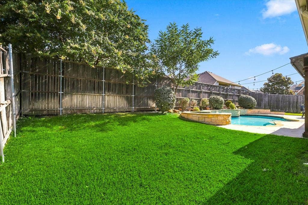 509 Wentworth Lane, Murphy, TX 75094 Expansive backyard featuring a manicured lawn, a swimming pool with integrated spa, a stone-accented perimeter, and mature landscaping