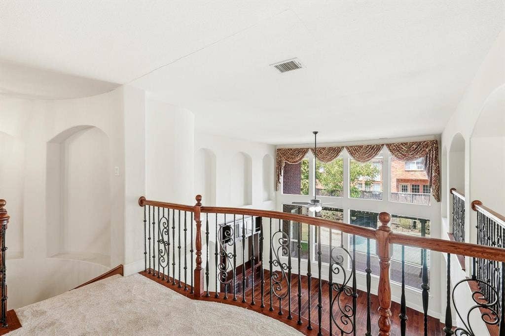 509 Wentworth Lane, Murphy, TX 75094 Second-story landing featuring curved wood and wrought iron balustrade, recessed wall niches, and a full-height window array with decorative valances