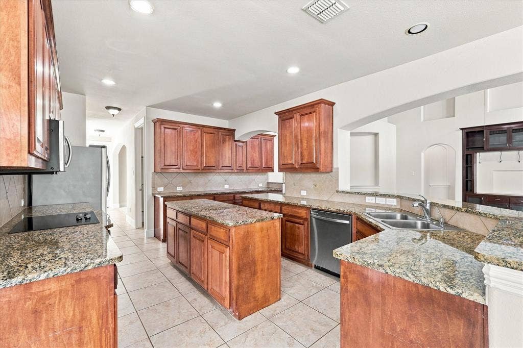 509 Wentworth Lane, Murphy, TX 75094 Kitchen featuring a central island, granite countertops, tile flooring, wood cabinetry, and stainless steel appliances