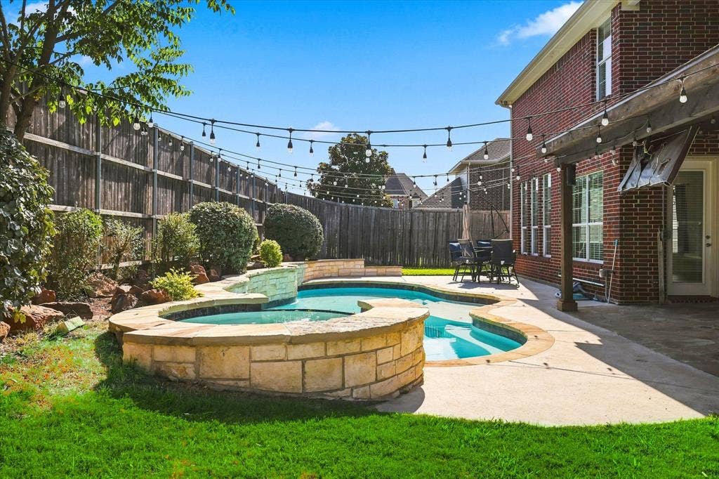 509 Wentworth Lane, Murphy, TX 75094 Custom-shaped swimming pool with an integrated spa, stone-clad perimeter, and waterfall feature