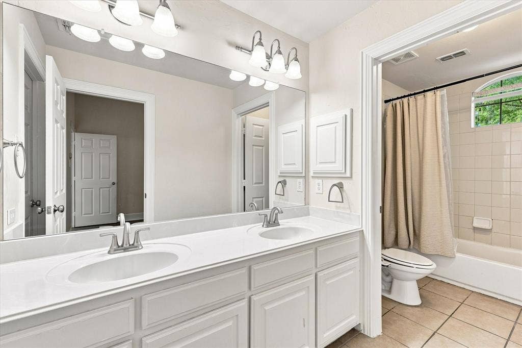 509 Wentworth Lane, Murphy, TX 75094 Dual vanity with integrated sinks and chrome fixtures, white tile flooring, and a tiled shower-tub combination with an arched window