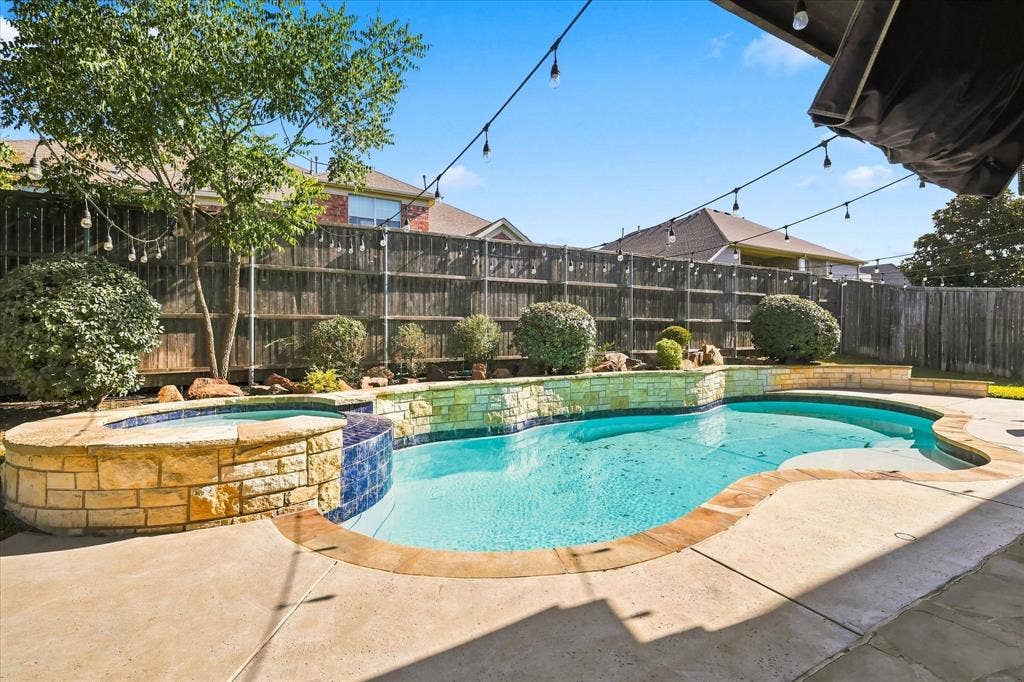 509 Wentworth Lane, Murphy, TX 75094 Outdoor swimming pool with integrated spa, stone-clad pool surround, concrete patio, and privacy fencing