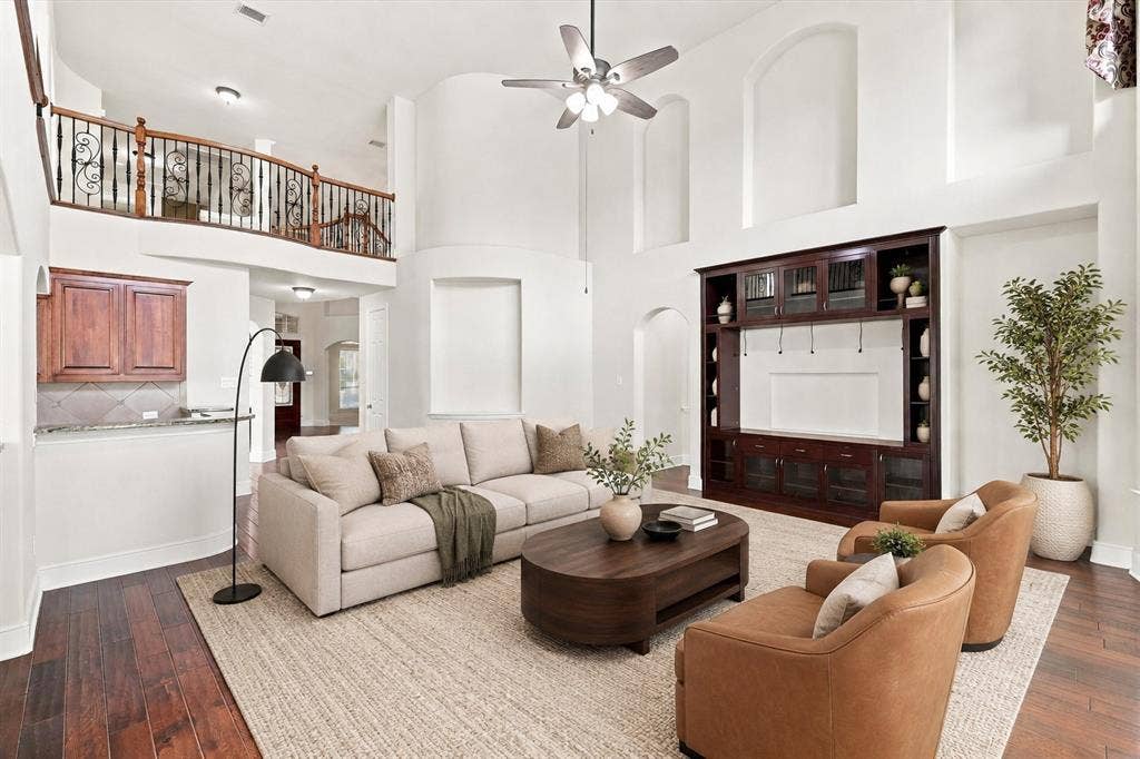 509 Wentworth Lane, Murphy, TX 75094 Virtually Staged Two-story living area with high ceilings, built-in media cabinetry, wood-finish flooring, and an upper-level balcony with wrought iron railing