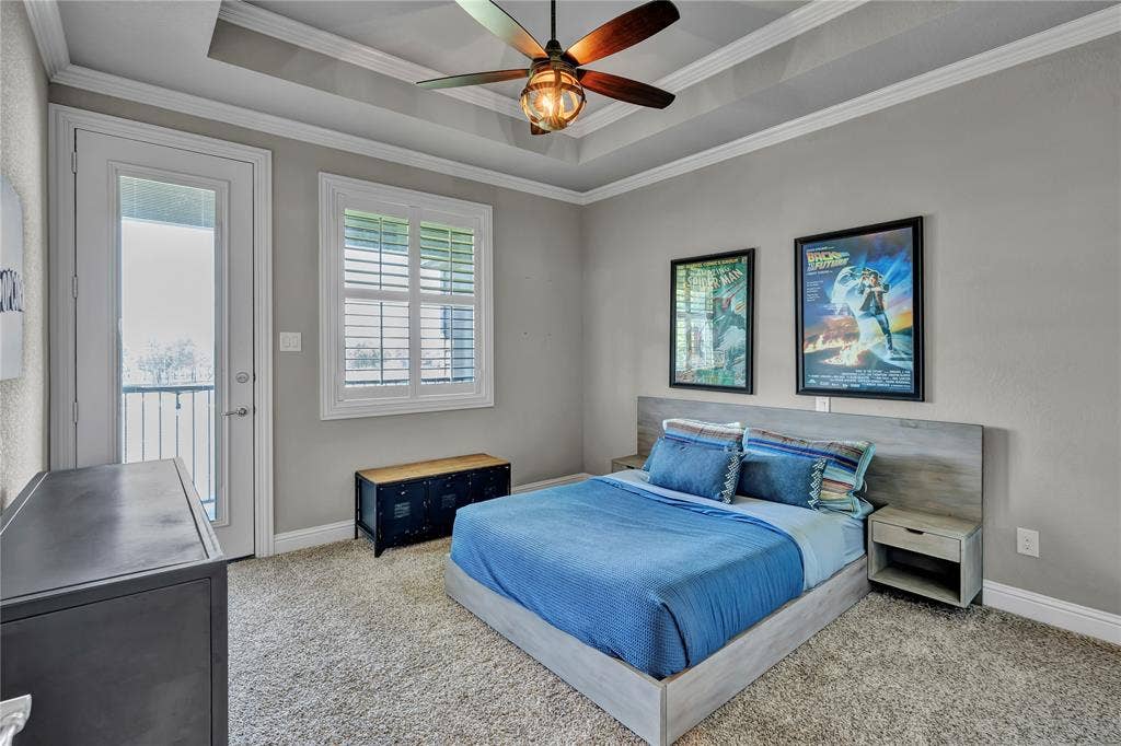 6412 Preferred Drive, Fort Worth, TX 76179 Carpeted bedroom featuring a tray ceiling with a built-in ceiling fan, crown molding, a glass-paneled door opening to a balcony, and a window with plantation shutters