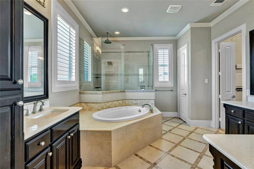 6412 Preferred Drive, Fort Worth, TX 76179 Spacious bathroom featuring an oval soaking tub, a glass-enclosed shower, and dual dark wood vanities with light countertops